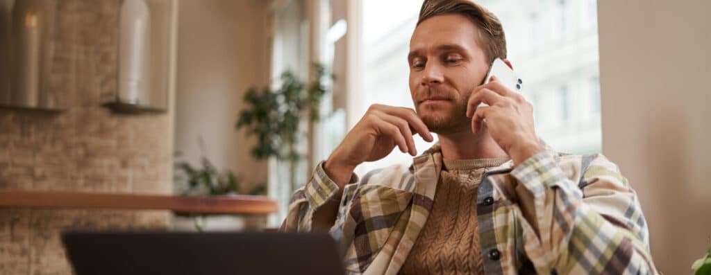 man sitting at home in front of laptop while on the phone