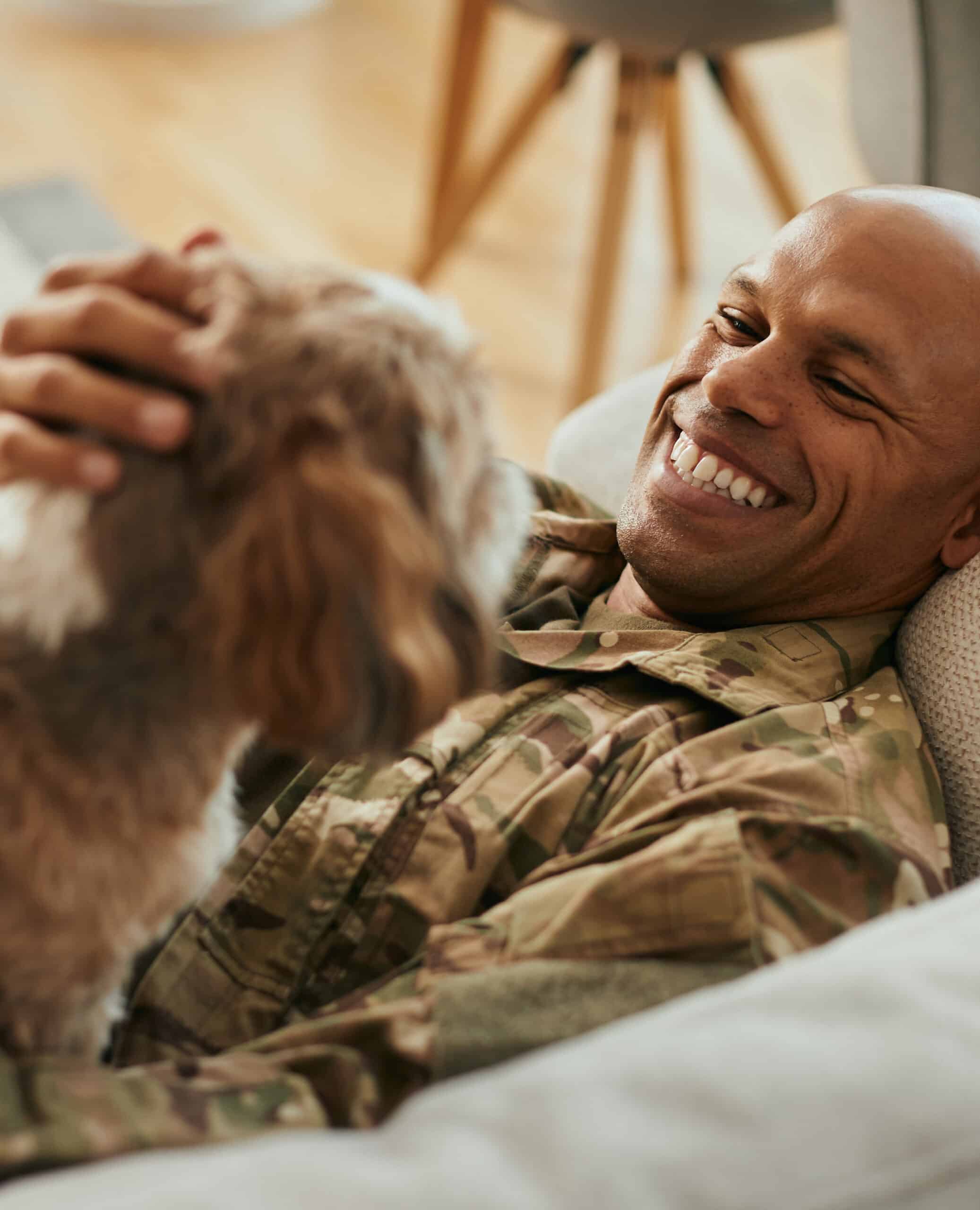 Happy African American military man enjoys with his dog at home.