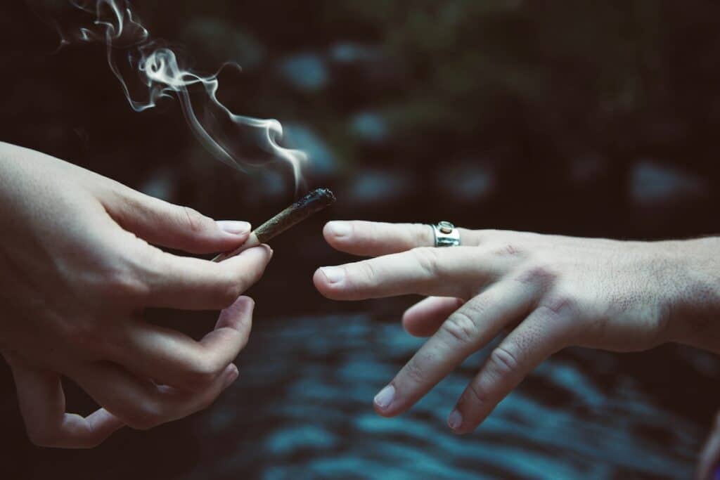 A hand passes a lit marijauna joint to another person.